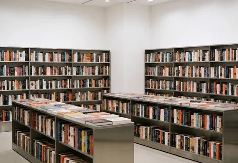 Modern bookstore interior featuring steel shelves, white walls, and books arranged in geometric patterns with bright lighting and a clean space.