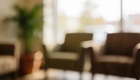 Comfortable chairs and a potted plant in a waiting area with warm lighting and soft bokeh, ideal for insurance or financial services text backgrounds.