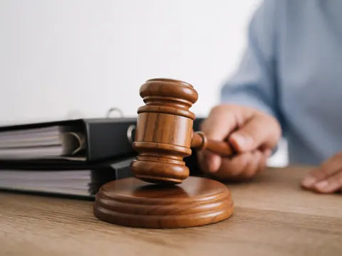 Close-up of a wooden judge gavel resting on a legal file folder on a desk in a sunlit office, symbolizing justice and legal proceedings.