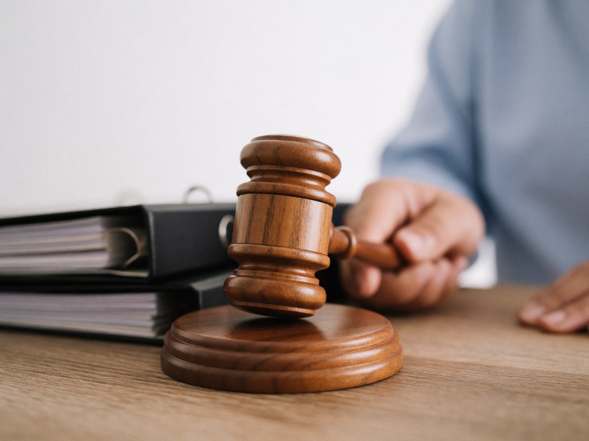 Close-up of a wooden judge gavel resting on a legal file folder on a desk in a sunlit office, symbolizing justice and legal proceedings.