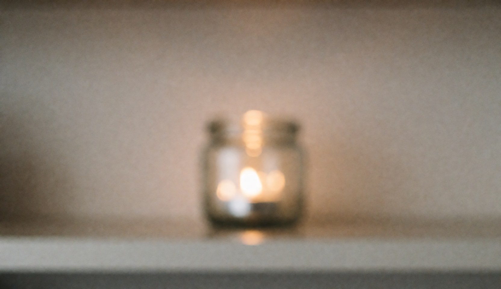 A lit candle in a glass jar on a soft spa background with warm lights and a relaxing atmosphere, ideal for wellness and massage text overlays.