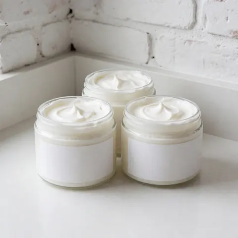 Three white textured cream jars displayed on a white countertop against a white brick wall with natural lighting for spa and massage products