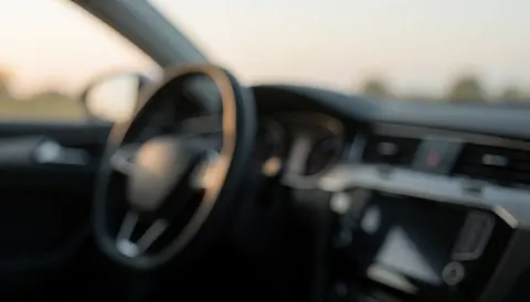 A soft-focus view of a car's interior featuring the steering wheel and dashboard, creating a calm and professional background suitable for text overlays.