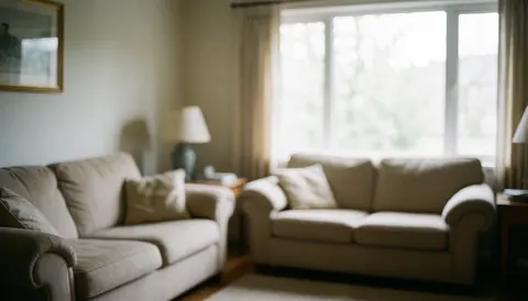 A spacious living room featuring beige sofas and a large window allowing natural light to illuminate the interior space.