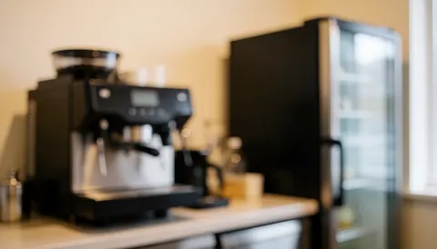 A cozy kitchenette interior featuring a coffee maker and refrigerator, illuminated by warm lighting, serving as a calm text background for insurance business content