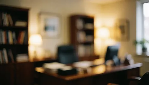 A calm professional office background featuring a wooden desk, bookshelf, warm lamp light, window, and plant, suitable for insurance text overlays