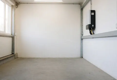 New solar inverter mounted on a white wall in a well-lit, empty workshop with concrete flooring, showcasing professional solar energy services.
