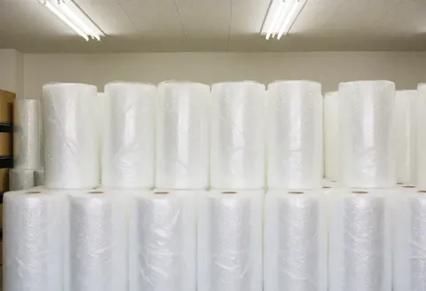 Rows of white bubble wrap rolls stacked in a clean, organized moving warehouse under bright fluorescent lighting, ready for packing furniture and items.