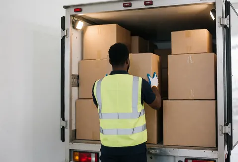 Professional mover wearing gloves and reflective vest organizing cardboard boxes in the back of a truck under work lights