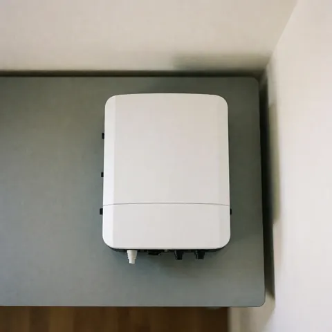 Compact white solar inverter with minimalist design on a gray surface, ideal for residential and small business installations, featuring clean uniform lighting.