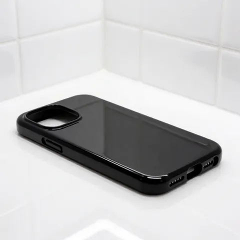 A sleek black protective phone case with a modern design rests on a clean white tiled surface, showcasing premium ceramic texture and subtle reflections for product marketing.
