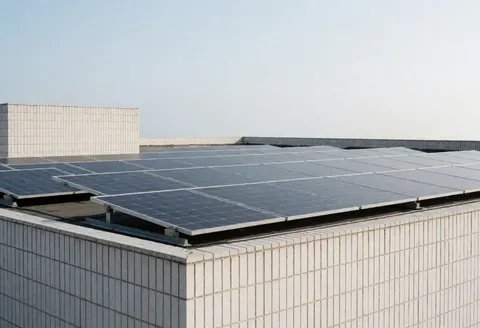 A wide view of solar panels mounted on the flat roof of a commercial building against a clear blue sky, showcasing renewable energy infrastructure.