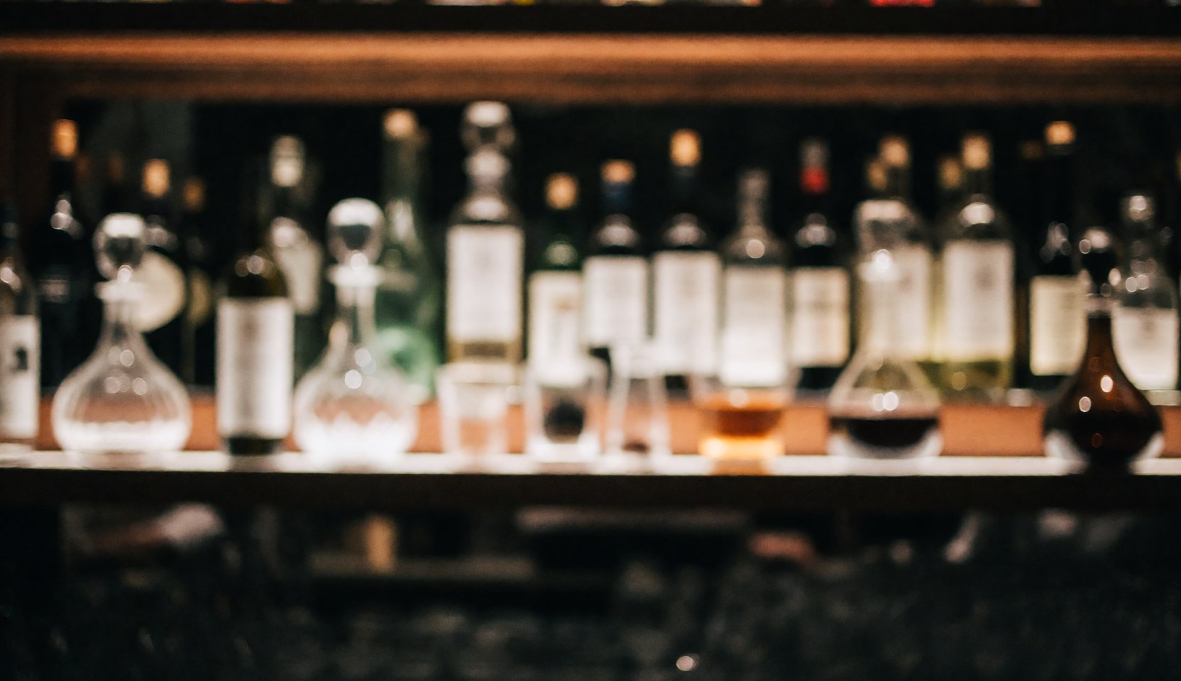 A dark and elegant hotel bar interior featuring wooden shelves stocked with liquor bottles and decanters, illuminated by warm bokeh lights, ideal for text overlays and business advertising.