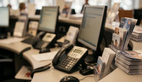 Travel agency workspace featuring computer monitors, telephones, and brochures on a blurred background suitable for text overlay