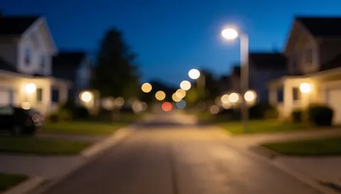 A quiet residential street at night featuring soft bokeh lights from streetlamps and house windows against a dark blue sky, serving as a secure background for text.