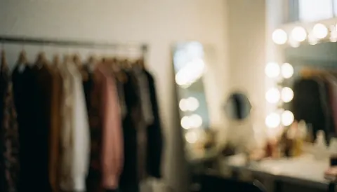 Soft blurred background of a dressing room with hanging clothes and studio lights, ideal for text overlay