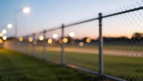 Metal fence background with blurred street lights at sunset, suitable for business security and perimeter protection text overlays.