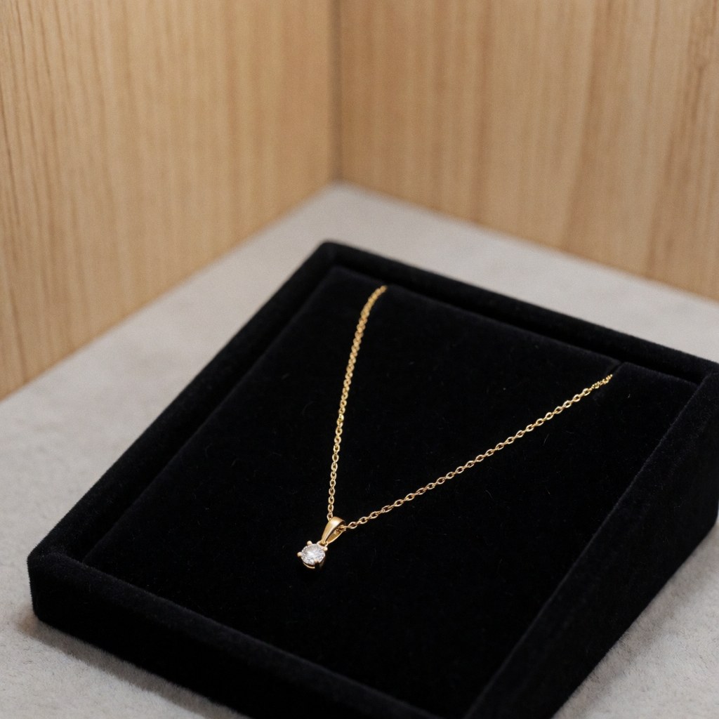Gold diamond necklace displayed in a black box on a light wood background, ideal for jewelry store product presentations