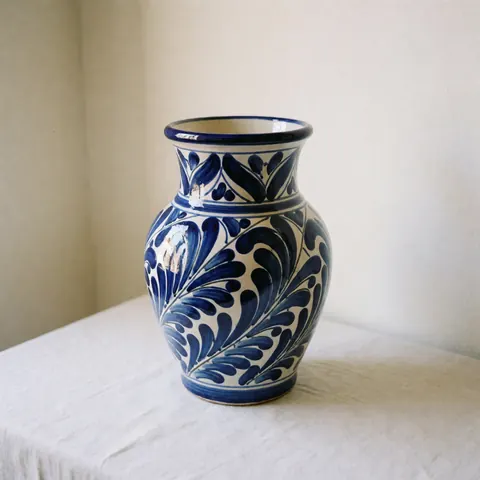 Blue and white Talavera ceramic vase with patterns on a white tablecloth against warm walls with natural lighting