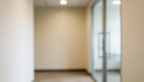 Softly blurred beige office hallway with glass doors, providing a neutral professional background suitable for business text and logos