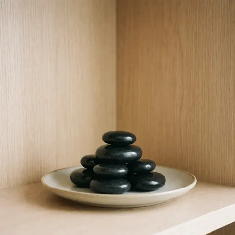 Smooth black volcanic stones arranged on a beige ceramic plate placed on light wood for a relaxing spa treatment