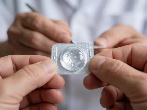 Hands holding a contact lens blister pack with water droplets on a clean, blurred background, ideal for optical care and vision health.