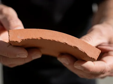 Detailed view of a curved ceramic roof tile showing the rough clay texture and earthy tones typical of hardware store building materials