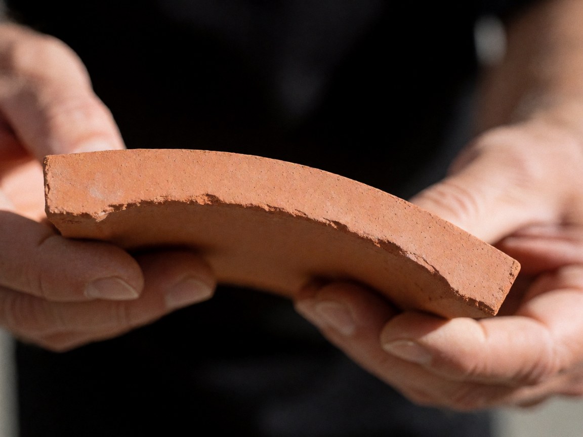 Detailed view of a curved ceramic roof tile showing the rough clay texture and earthy tones typical of hardware store building materials