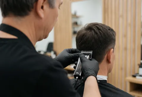 Barber wearing black gloves cutting hair with electric clippers in a wood-paneled shop