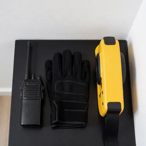 Professional security gear including radio, gloves, and retractable barrier on a dark surface, suitable for security service catalogs