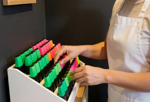 Close-up of hands arranging vibrant bookmarks on a white display stand in a bookstore with warm lighting and a gray wall background