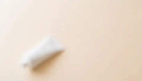 Soft blurred beige background with a cream tube in the corner, ideal for beauty service text and web design.