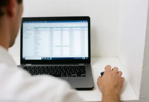 Back view of a consultant analyzing data on a laptop with a mouse in hand in a professional office setting