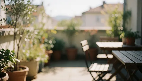 A bright sunlit outdoor terrace featuring light wood furniture, potted plants, and a calm atmosphere suitable for real estate text backgrounds