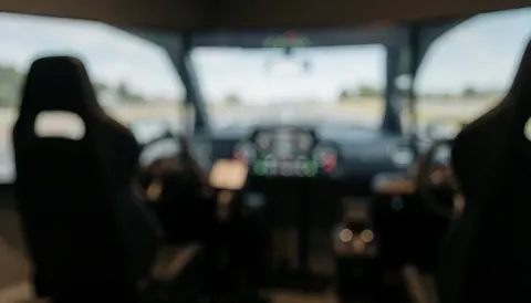 A blurred background image of a driving simulator interior featuring a dashboard, seats, and a window view, suitable for educational or automotive training contexts.
