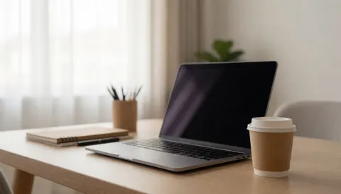 A clean office desk setup featuring a laptop, notebook, pen, and coffee cup near a window with natural light, ideal for educational or business text overlays