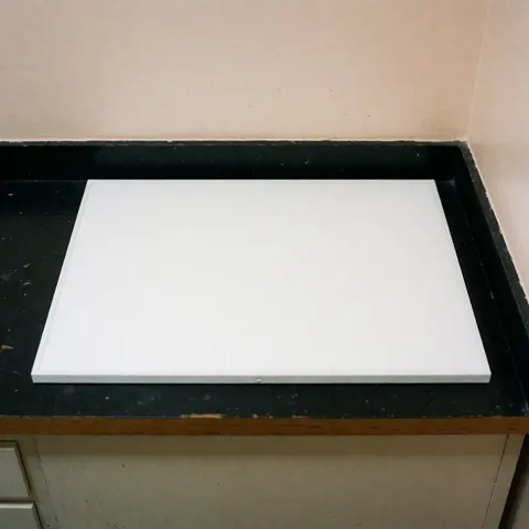 A clean white rectangular replacement air conditioning filter lying on a work surface, ready for installation or maintenance.