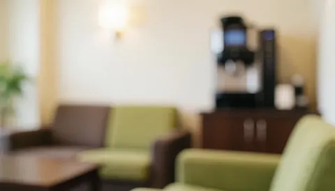 Softly blurred background of a comfortable office break room featuring a sofa, coffee machine, and warm lighting in neutral tones.