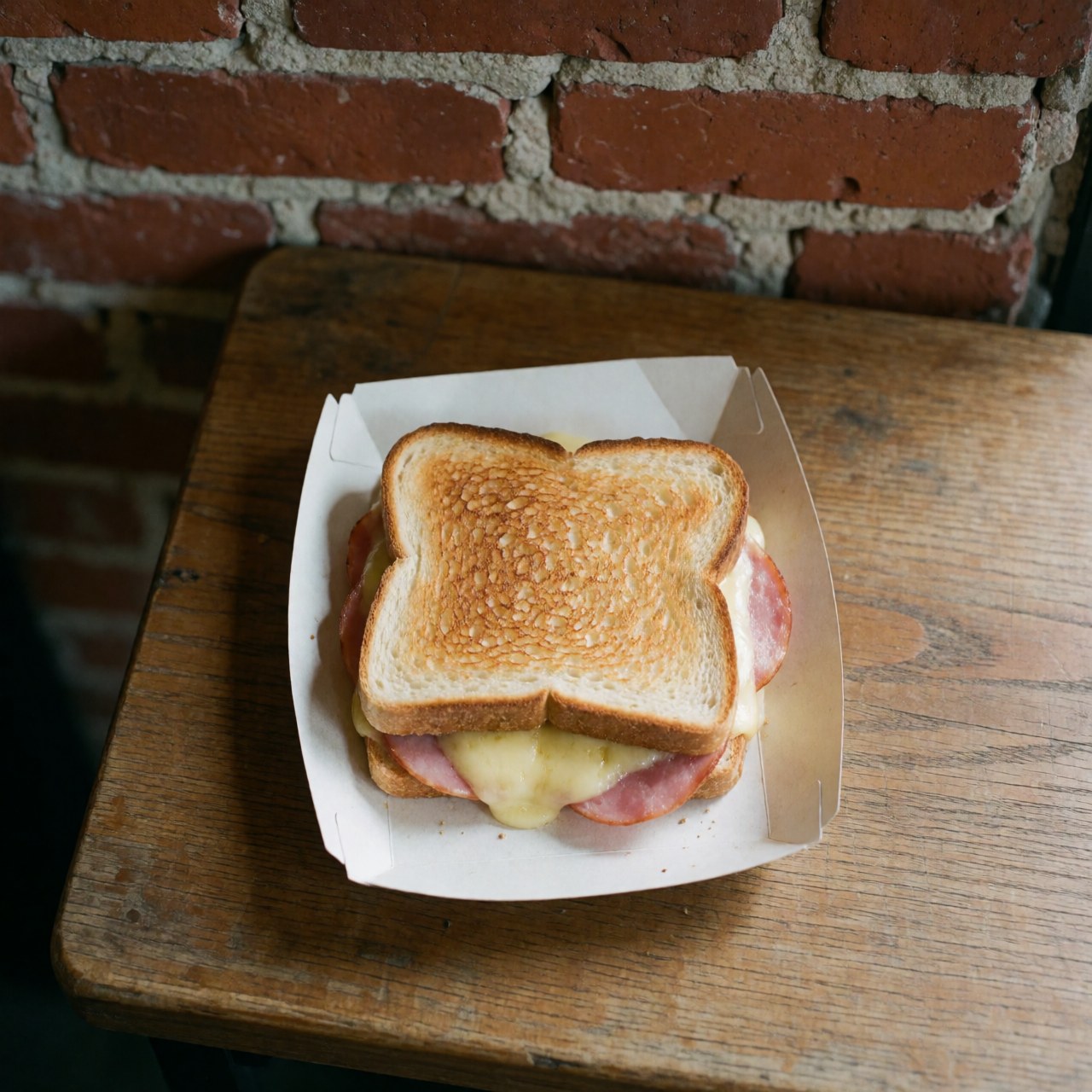 Top down view of a toasted ham and cheese sandwich on a wooden surface with a brick background