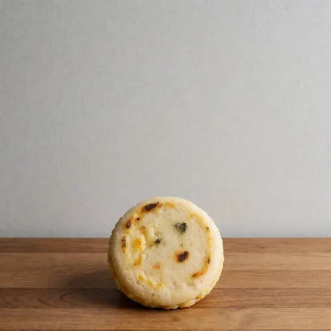Top view of a small arepa with melted cheese on a wooden surface against a light gray wall, representing fast food.