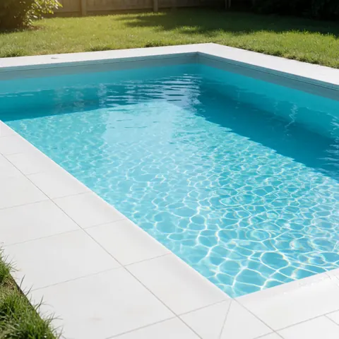 Brand new finished inground swimming pool featuring bright turquoise water, white tiles, and green lawn under intense sunlight, ideal for promoting construction services.