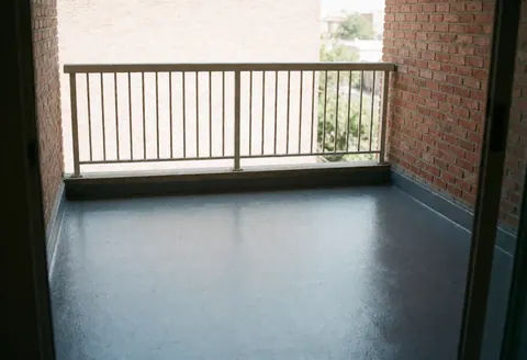 A clean and new finished balcony featuring a brick wall, metal railing, and large windows with natural light, suitable for construction and real estate projects