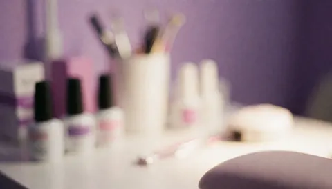 Soft focus background of a nail salon featuring beauty products, tools, and purple and white tones, ideal for text overlays and promotional designs.