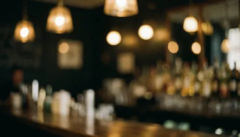Warmly lit bar interior with soft bokeh lights, creating a cozy and sophisticated atmosphere ideal for promotional text overlays.