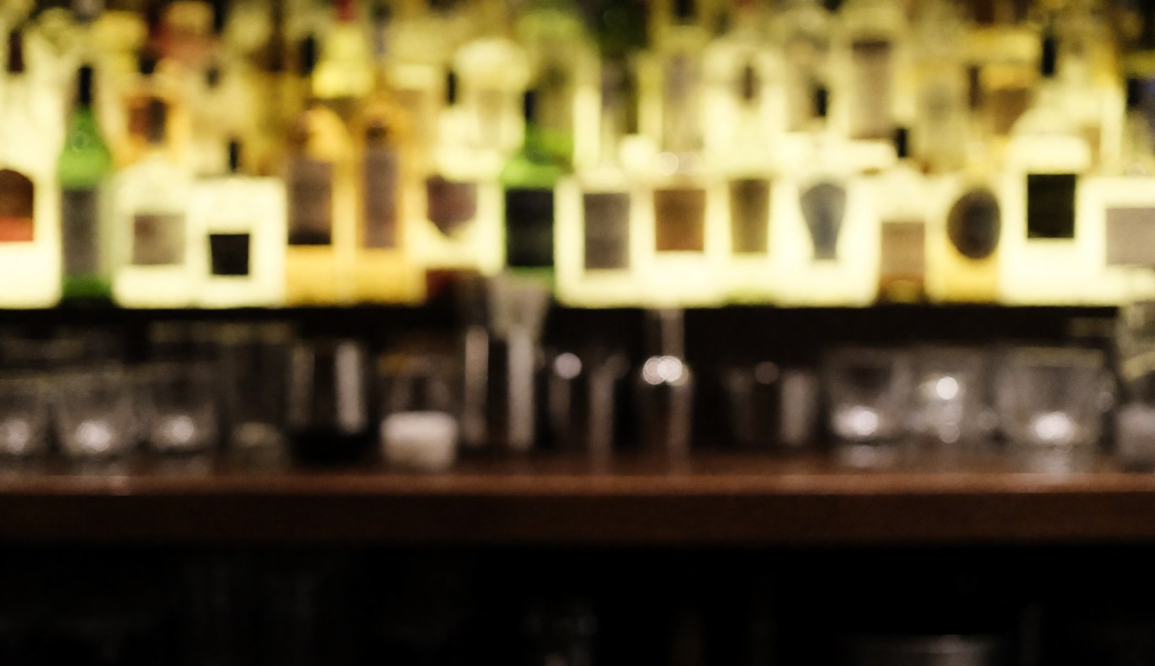 Warmly lit bar background featuring out-of-focus bottles and glasses, ideal for advertising text or website design.