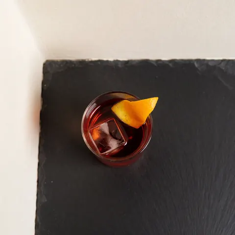 Top-down view of a Negroni cocktail in a rocks glass with ice and an orange slice on a dark table