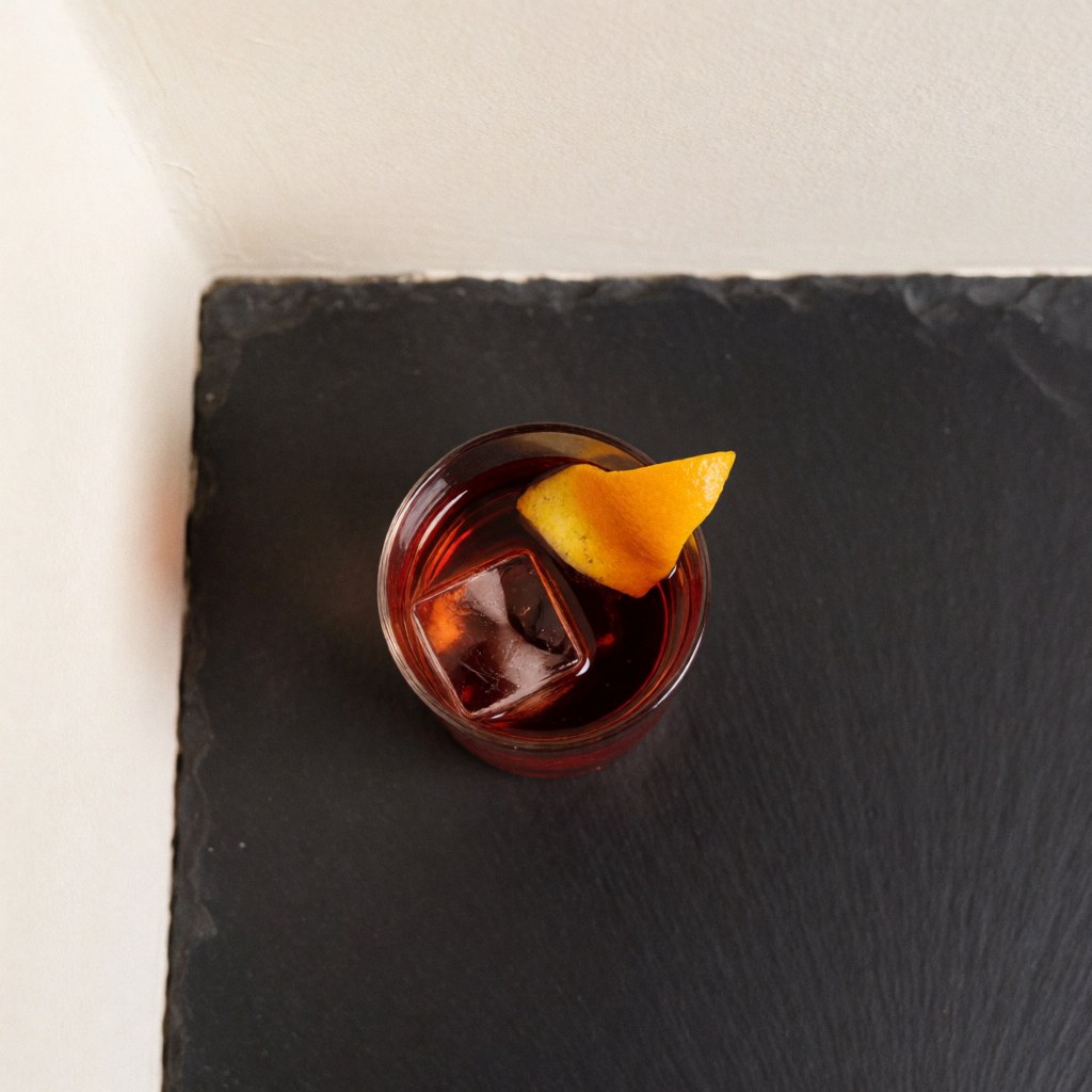 Top-down view of a Negroni cocktail in a rocks glass with ice and an orange slice on a dark table