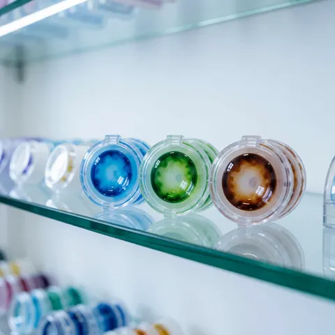 Colorful contact lenses displayed on a glass shelf in a modern optical store with a blurred background of other vision care products.