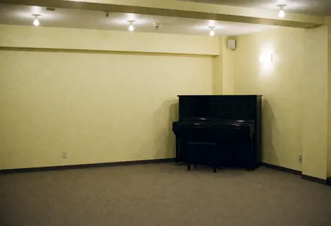 Empty bar interior featuring a black piano in the corner, pale yellow walls, and warm lighting, creating an inviting atmosphere for musical events.