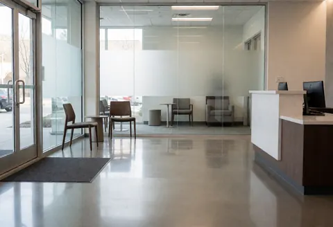 Bright modern office interior featuring a reception desk, chairs, polished concrete floor, and glass walls, ideal for cleaning service marketing.